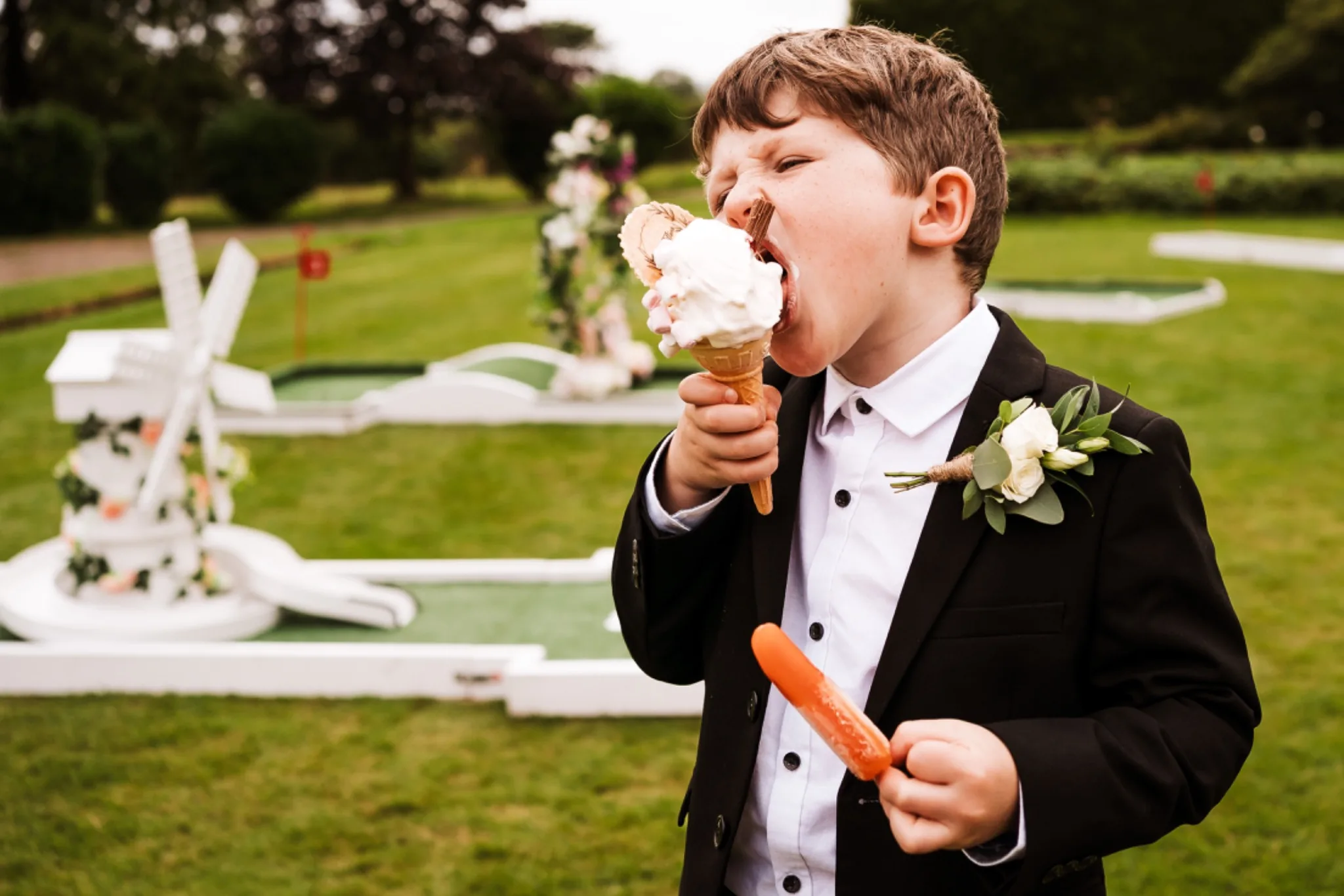Young wedding guest in a suit enthusiastically eating an ice cream during an outdoor wedding reception.
