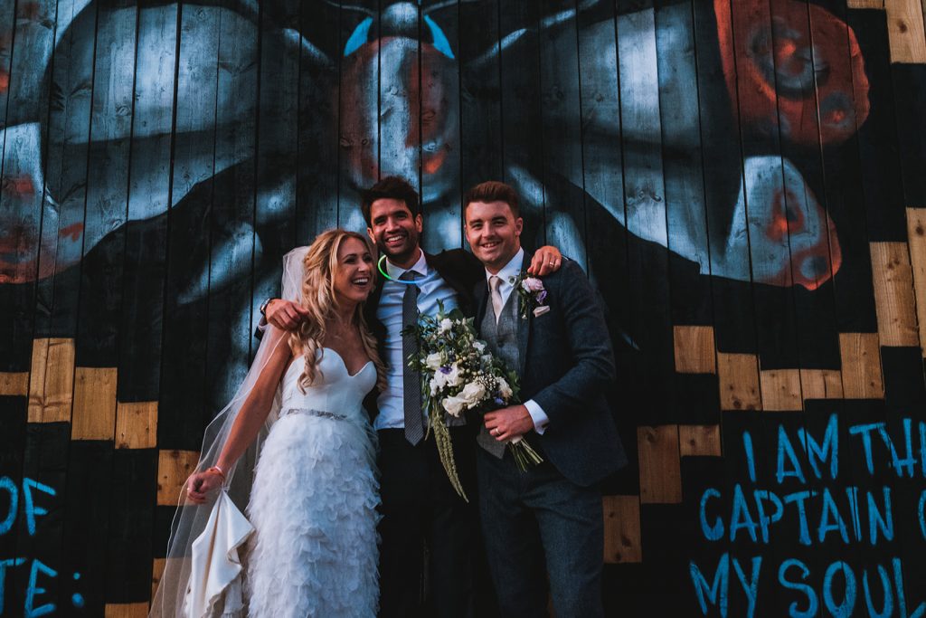 Three people laughing in front of graffiti wall art.